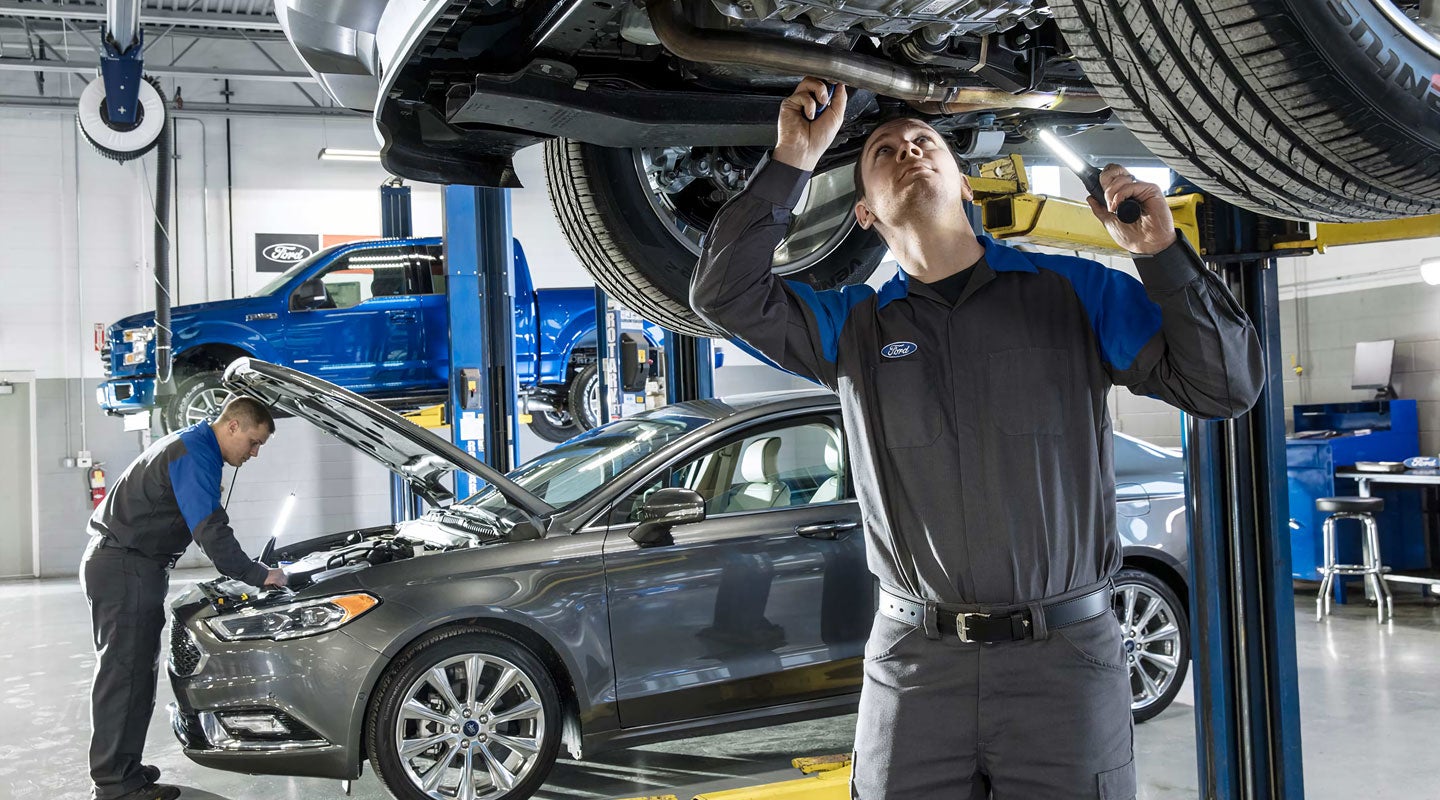 Two Ford mechanics in a garage inspecting vehicles on hydraulic lifts