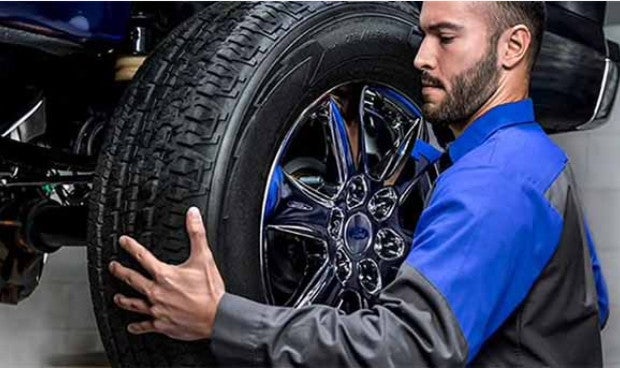 A Ford technician installing a large tire on a vehicle's chrome rim