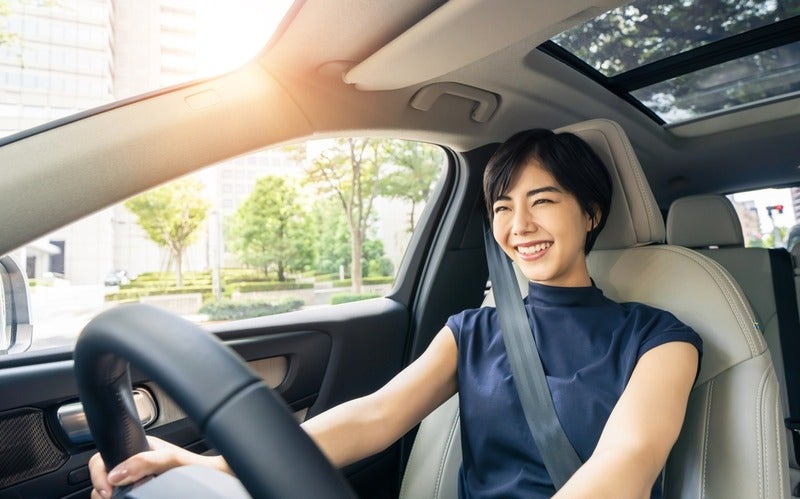 Smiling woman driving a modern vehicle with a large panoramic sunroof.
